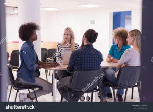 Five individuals having a conversation while sitting at a desk