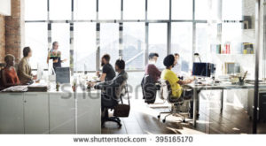 Eight people working in an office in front of a wall of windows